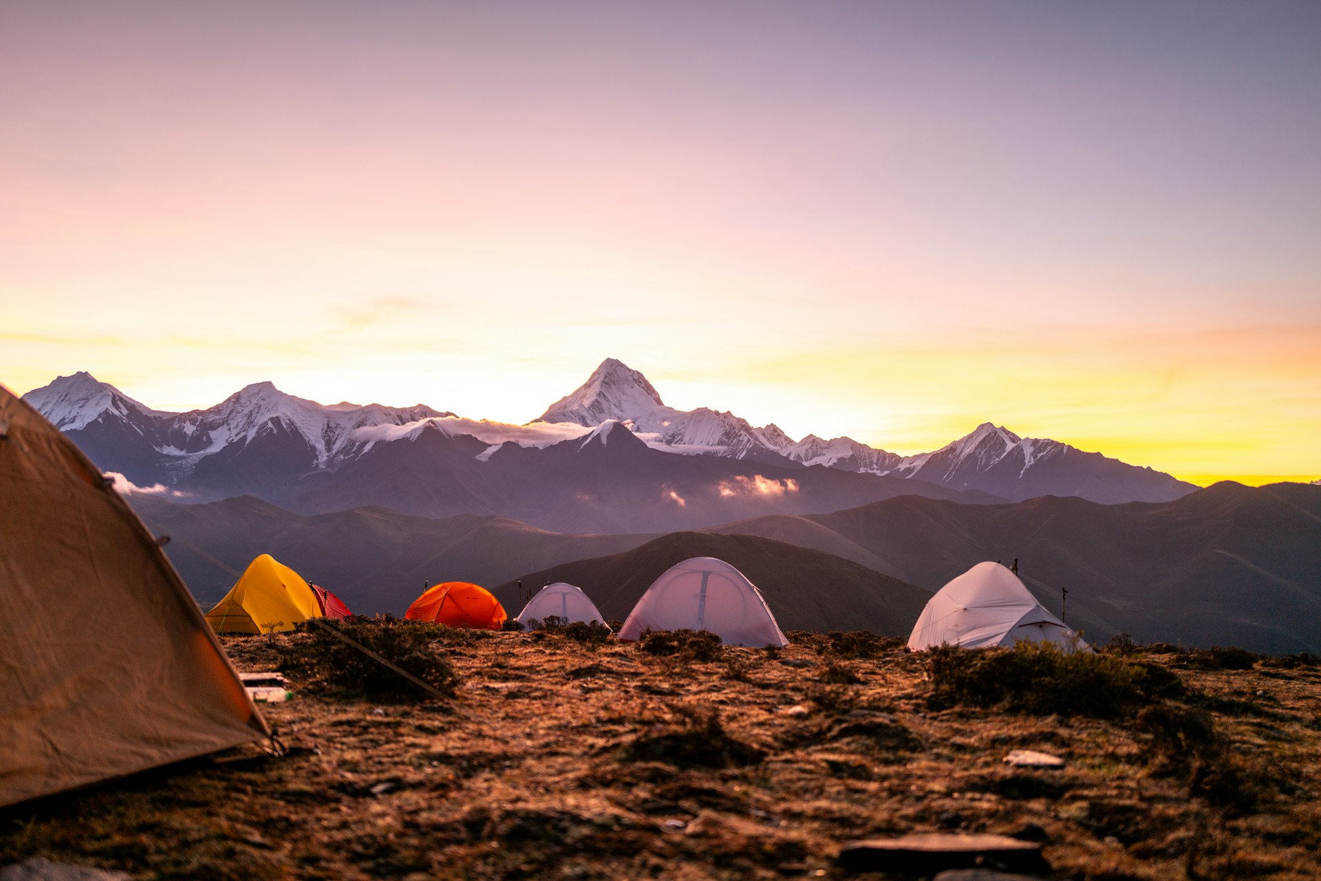 Tents set up on a rocky mountain landscape at sunset.